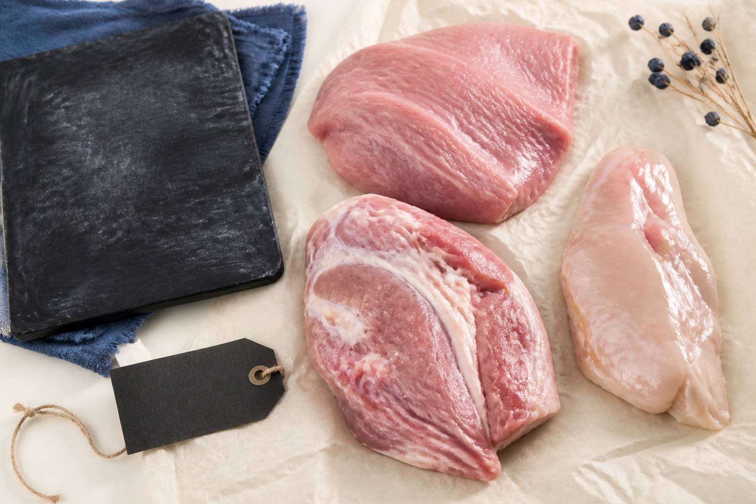 Gros plan de morceaux de veau cru séparés — épaule claire, tendron gras et collier — sur papier de boucherie