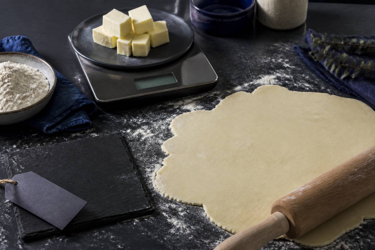 Farine et beurre pesés sur une balance de cuisine avec une pâte brisée étalée
