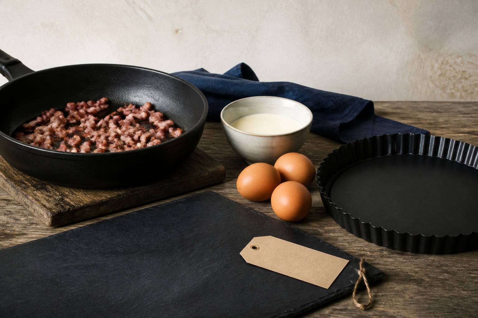 Ingrédients de quiche lorraine — lardons, œufs et crème — sur un plan de travail avec un moule