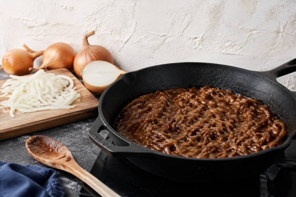 Compotée d'oignons caramélisée brun ambré dans une grande poêle en fonte